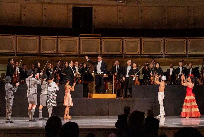 A wide shot of the CSO and conductor Harry Bicket bowing as The Joffrey Ballet dancers applaud them from on stage