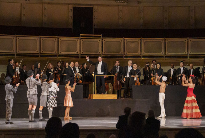 A wide shot of the CSO and conductor Harry Bicket bowing as The Joffrey Ballet dancers applaud them from on stage