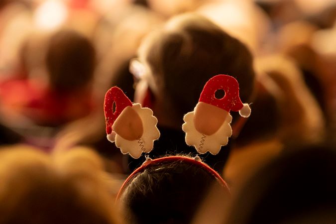 A closeup shot of a Santa Claus headband worn by a child sitting in the audience