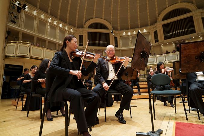 associate concertmaster Stephanie Jeong and assistant concertmaster David Taylor smile for the camera during warm-ups