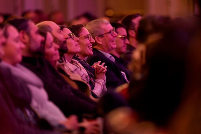 the audience on the main floor laughs at a story Chris Thile is telling