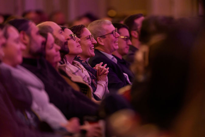 the audience on the main floor laughs at a story Chris Thile is telling