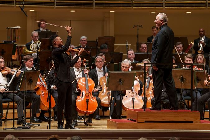 Group shot of violinist Randall Goosby, conductor Sir Mark Elder and several CSO cello musicians