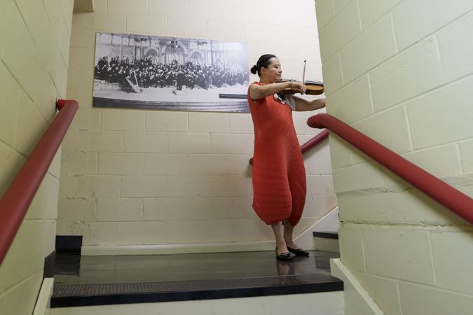 Teng Li warms up on her viola backstage in front of an old, black-and-white portrait of the orchestra