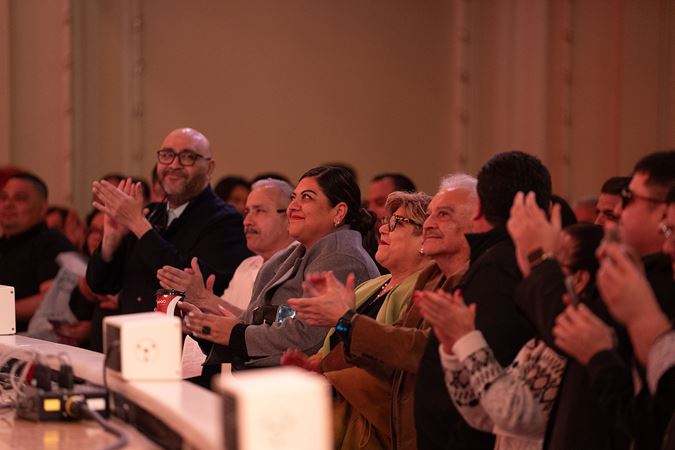 audience members in the front row rise to their feet and clap for Trío Remembranza