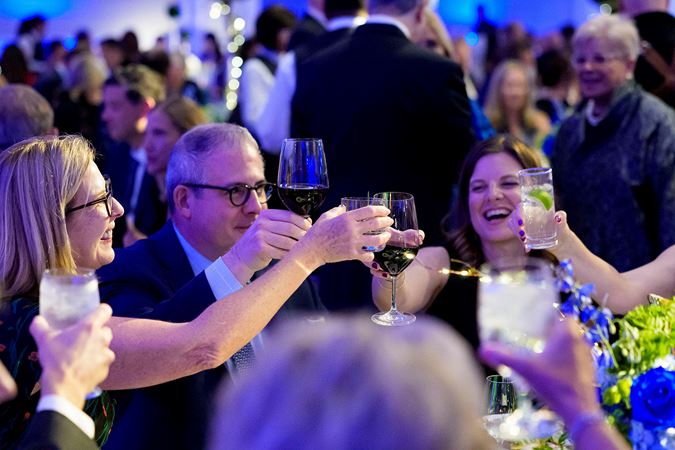 Closeup shot of gala attendees smiling and raising their glasses for a cheers