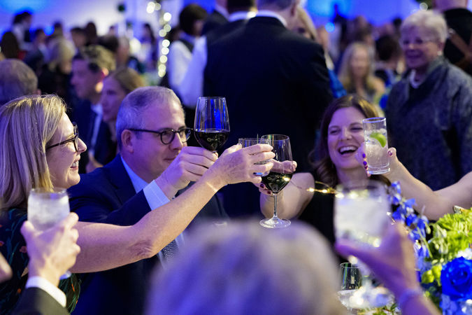 Closeup shot of gala attendees smiling and raising their glasses for a cheers