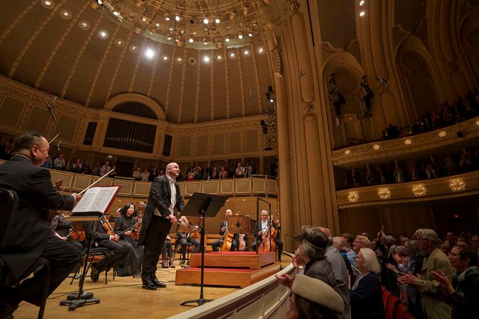 Side wide shot of CSO principal trumpet Esteban Batallán bowing on stage and the audience applauding