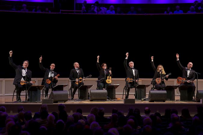the seven ensemble members raise their arms after their final strum