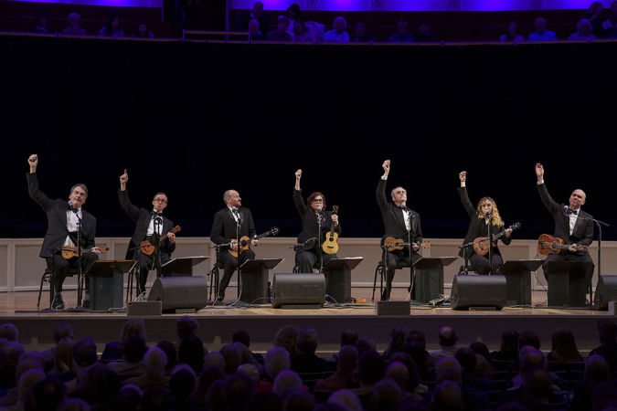 the seven ensemble members raise their arms after their final strum