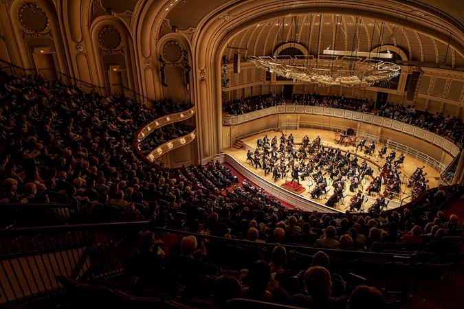 a wide shot from the point of view of the audience in the upper balcony, looking out over the stage and the enraptured crowd