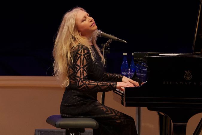 Eliane Elias sits at the piano, her head thrown back and blonde hair waving mid-performance