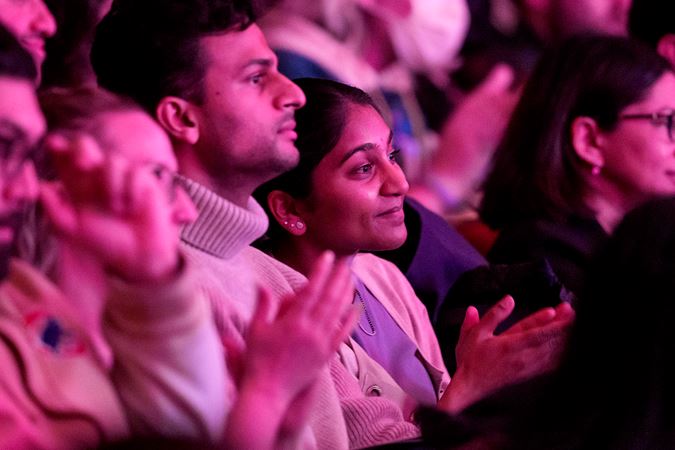audience members clap, awash in a pink glow from the stage lighting