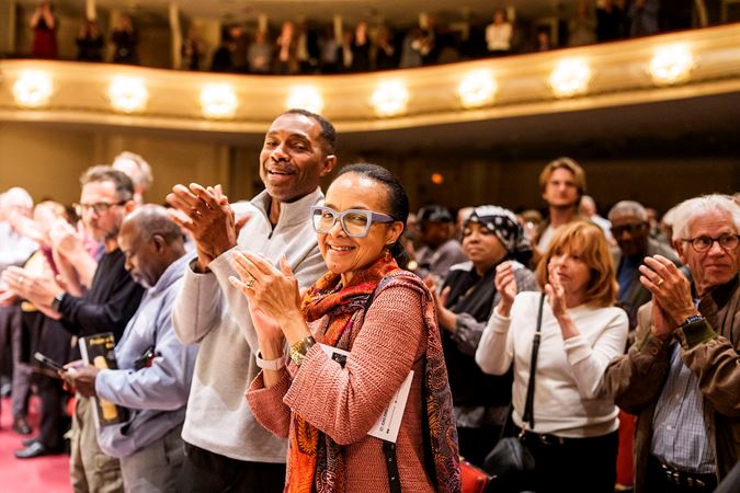 audience members in the front row smile at the camera during a standing ovation