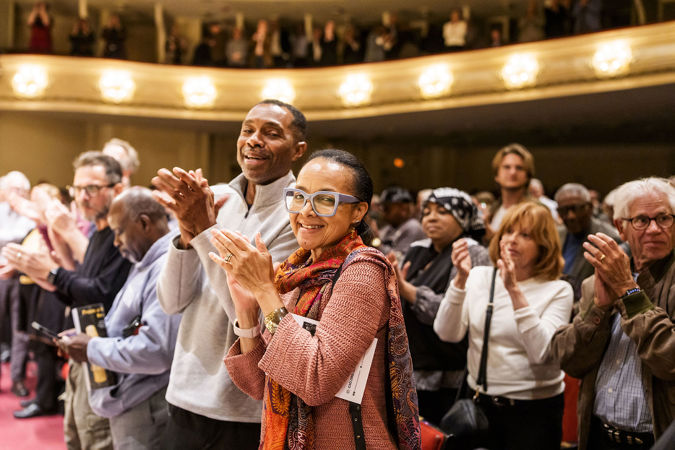 audience members in the front row smile at the camera during a standing ovation