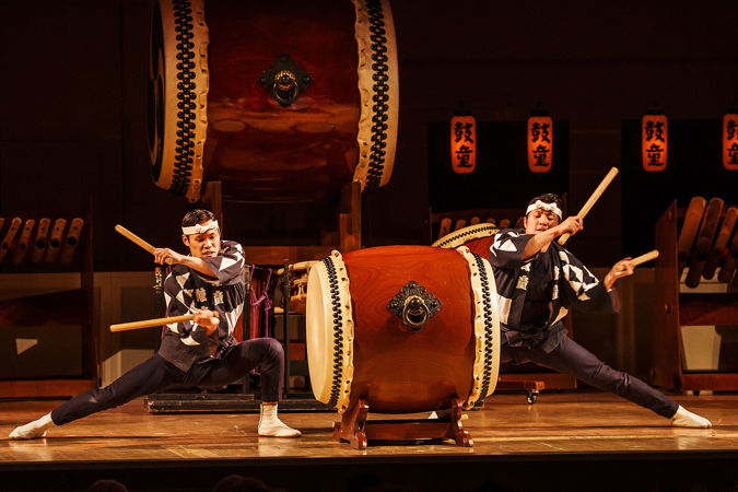 two Kodo members beat different sides of the same drum