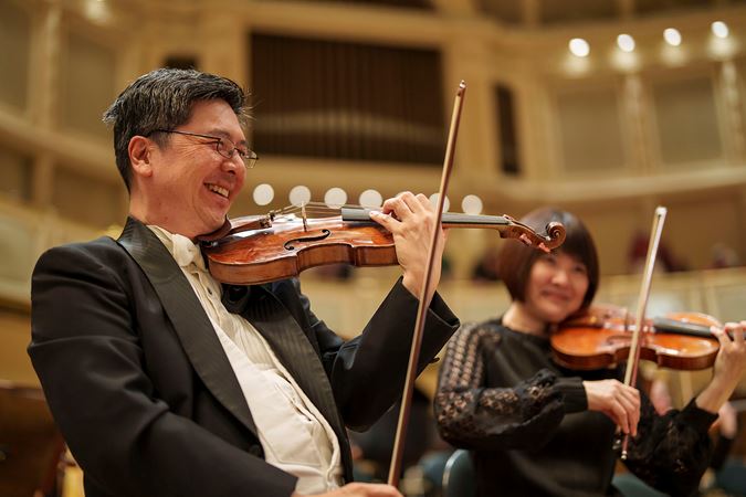 CSO violin Cornelius Chiu smiles wide for the camera during warm-ups