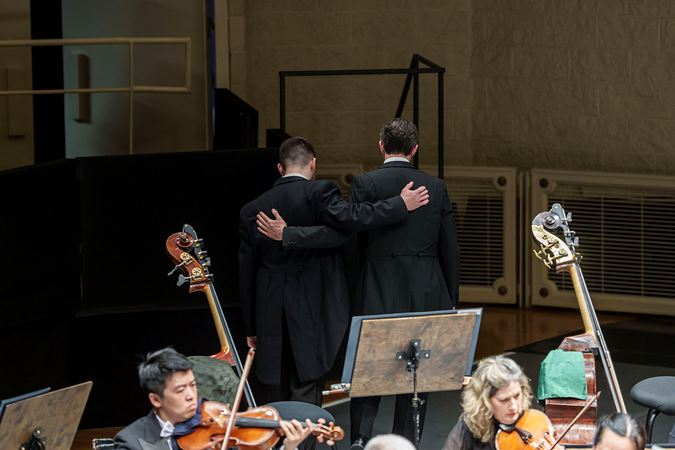 Closeup of two bass players embrace each other as they walk off stage during the last movement of Haydn's Farewell Symphony