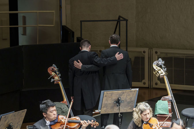 Closeup of two bass players embrace each other as they walk off stage during the last movement of Haydn's Farewell Symphony