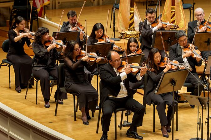 The violin section, led by concertmaster Robert Chen, plucks its strings in unison