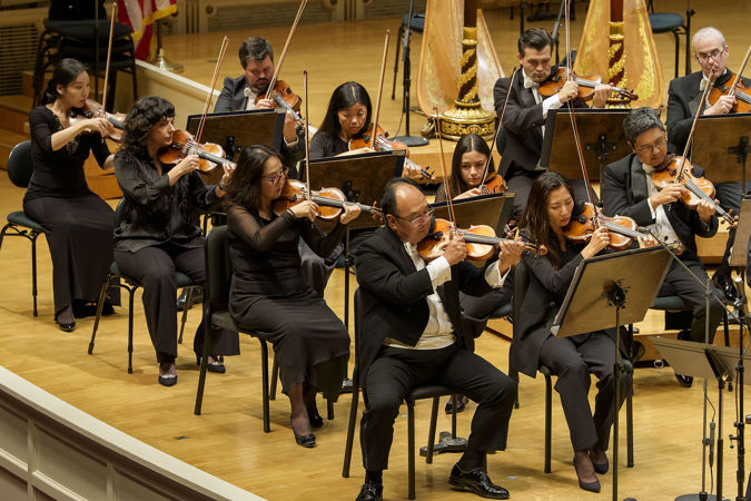 The violin section, led by concertmaster Robert Chen, plucks its strings in unison