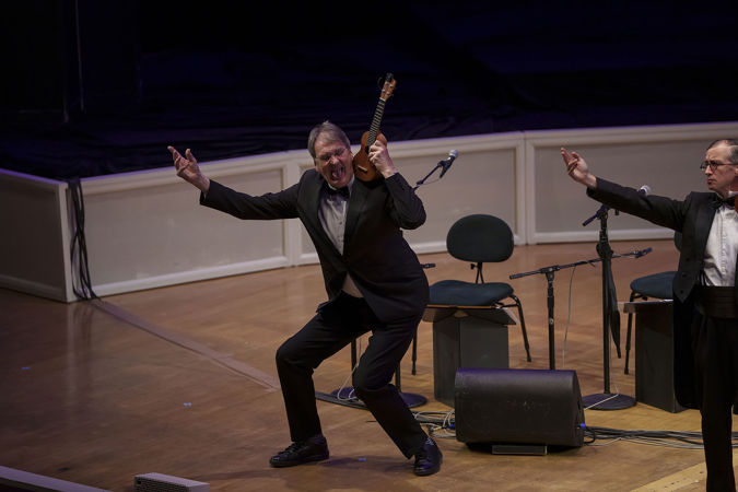 ensemble member Peter Brooke Turner strikes a silly pose with his tongue out and ukulele raised to his ear