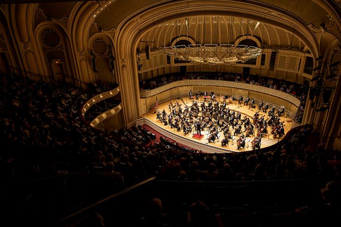 A wide shot of the orchestra in action from the right side of the upper balcony