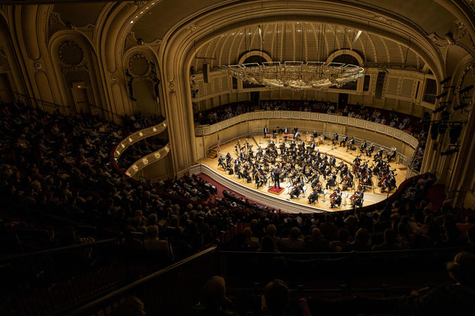 A wide shot of the orchestra in action from the right side of the upper balcony