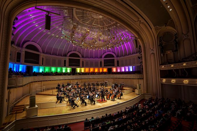 Wide shot of members of the Chicago Symphony Orchestra and conductor Daniel Bartholomew-Poyser performing on stage