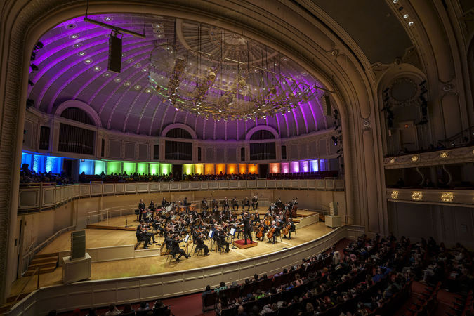 Wide shot of members of the Chicago Symphony Orchestra and conductor Daniel Bartholomew-Poyser performing on stage