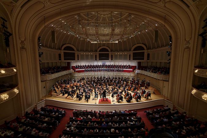 A wide shot of Zell Music Director Designate Klaus Mäkelä leading the Chicago Symphony Orchestra and Chorus and Uniting Voices Chicago