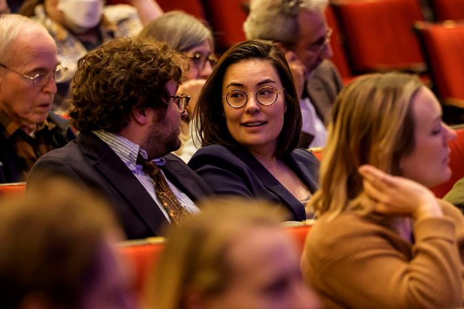 two audience members wearing glasses chat in their seats before the concert