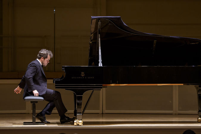Benjamin Grosvenor sits expressively at the piano bench, hands thrown back after finishing a piece