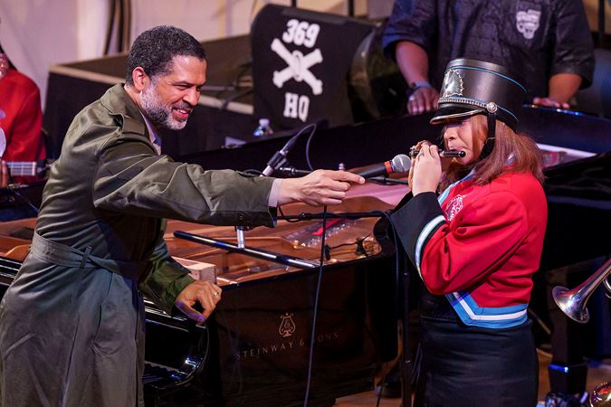 Jason Moran holding a microphone for a Kenwood Academy High School Marching Band flute player soloing