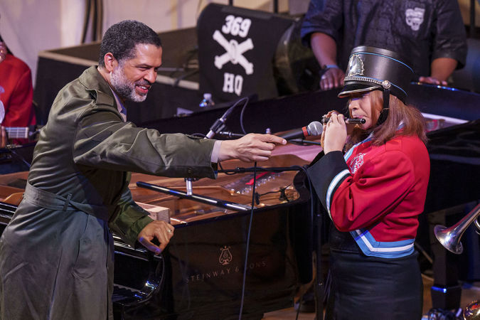 Jason Moran holding a microphone for a Kenwood Academy High School Marching Band flute player soloing