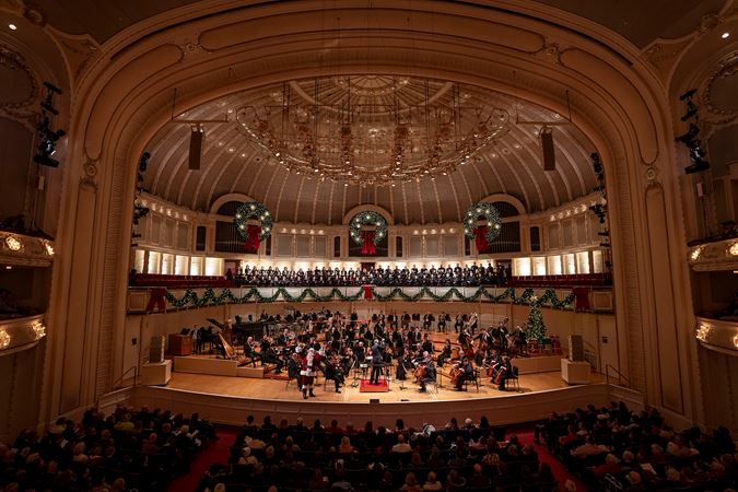Wide shot of members of the Chicago Symphony Orchestra and Chorus, conductor Alastair Willis and Santa Claus on stage