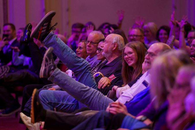 audience members laugh and kick their legs in the air during a comedic audience participation moment