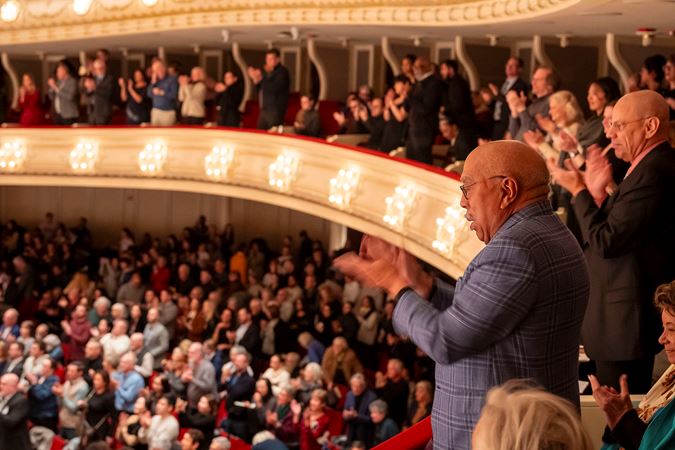 A sideview of patrons applauding from the box level