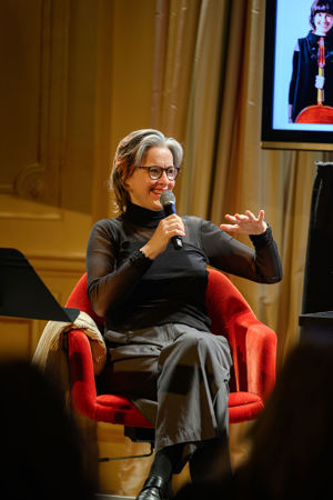 wearing glasses and an all-black outfit, CSO cello player Katinka Kleijn smiles while she answers a question into the mic
