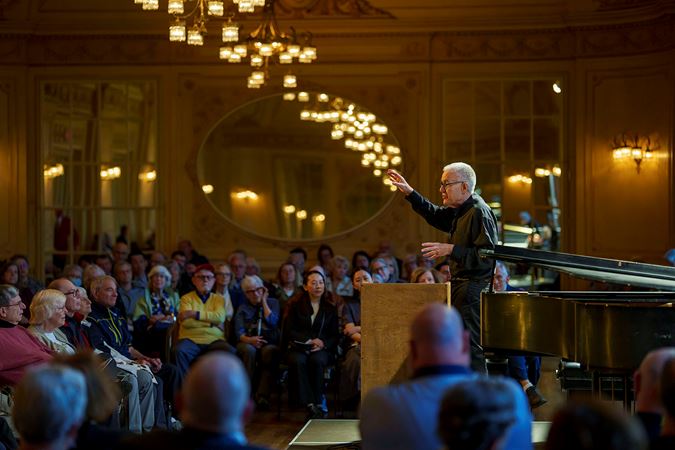 CSO viola Max Raimi stands behind a lectern in Grainger Ballroom as he gives a preconcert talk to inquisitive patrons