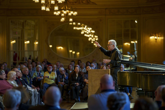 CSO viola Max Raimi stands behind a lectern in Grainger Ballroom as he gives a preconcert talk to inquisitive patrons