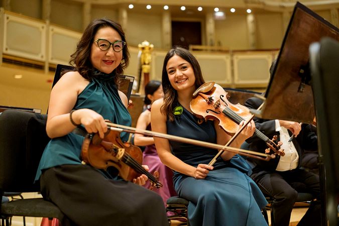 CSO assistant concertmaster Yuan-Qing Yu and violin Gabriela Lara smile at the camera before warming up on stage
