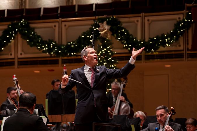 A closeup of conductor Alastair Willis inviting audiences to sing along to the music