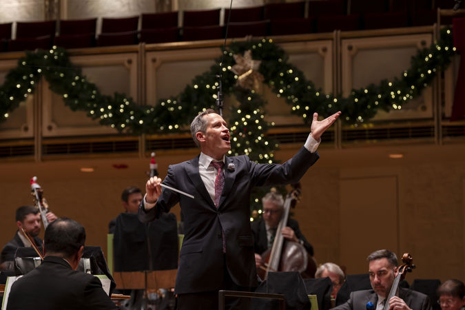 A closeup of conductor Alastair Willis inviting audiences to sing along to the music