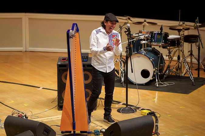 Edmar Castañeda laughs beside his harp while joyfully addressing the audience