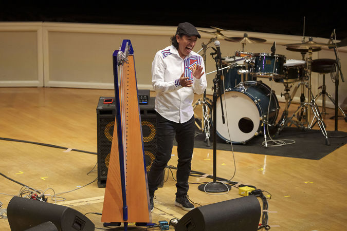Edmar Castañeda laughs beside his harp while joyfully addressing the audience