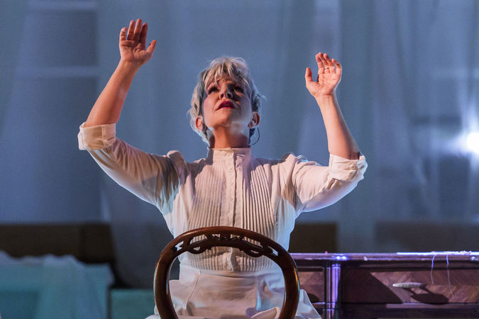 Joyce DiDonato sits on a backwards chair, hands and face raised to the sky during a dramatic pause in the performance