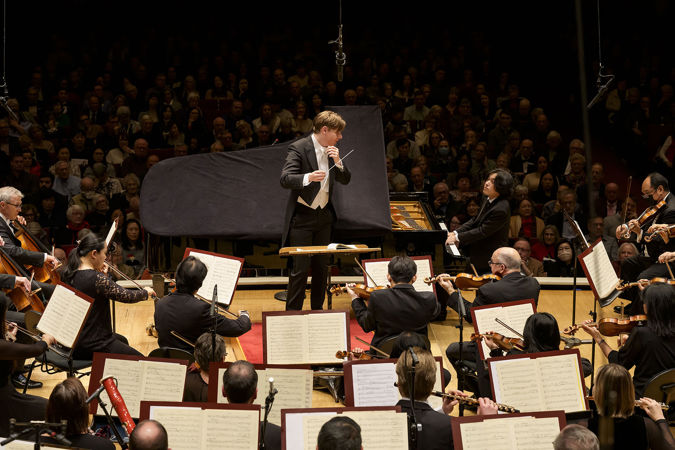 seated at the piano, Yunchan Lim looks up to Klaus Mäkelä on the podium for a cue