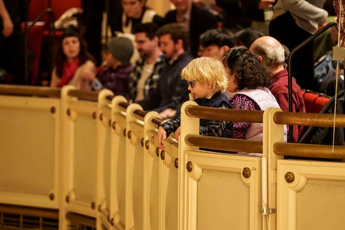a young audience member looks down in awe from the balcony