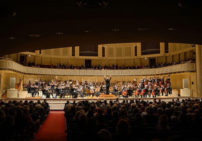 a point of view looking out over the heads of the audience from the back of the main floor, as the orchestra and cellist Gabriel Cabezas perform Lost Coast